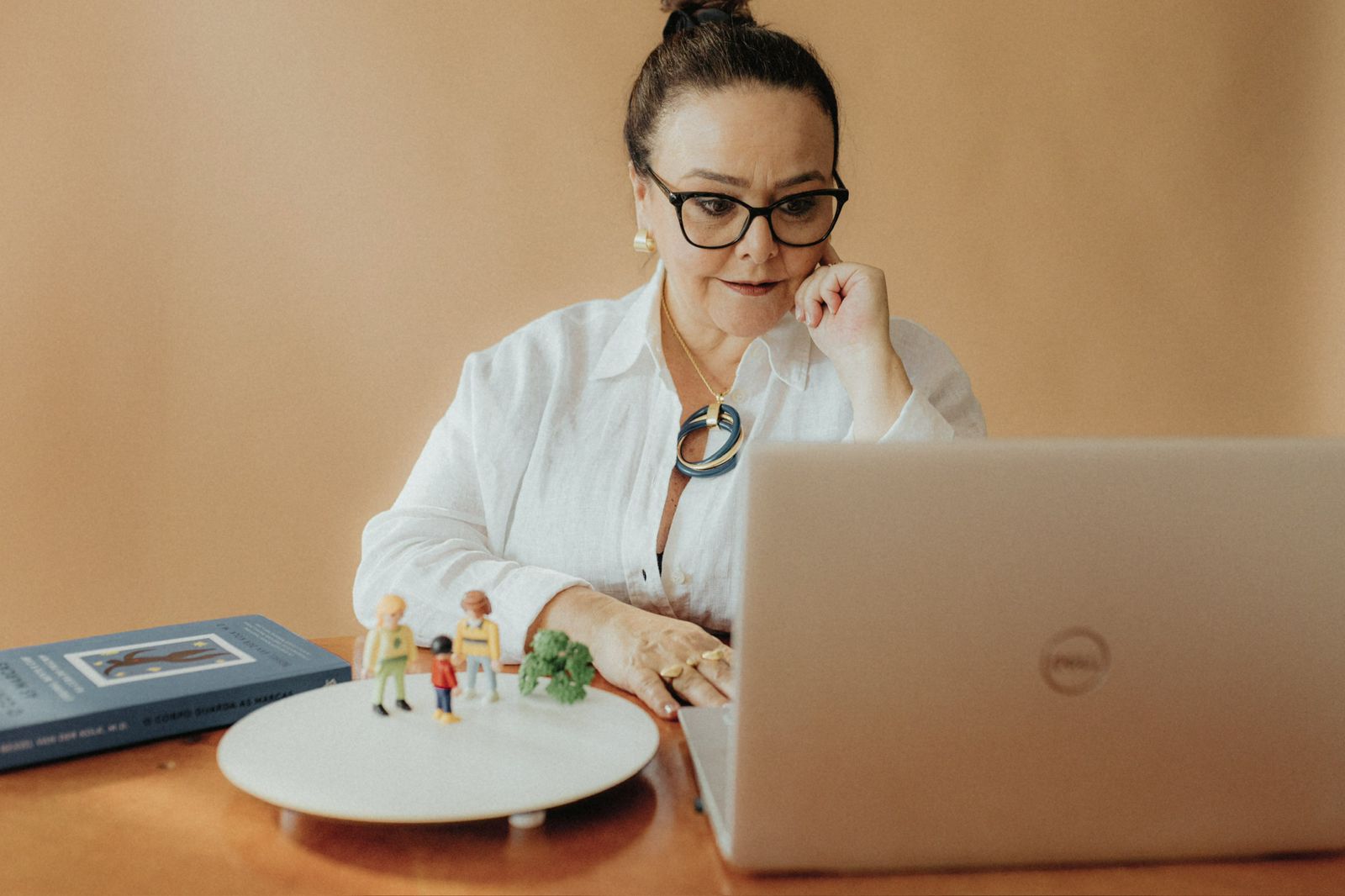 Claudia Gonçalves em sessão de constelação, com mesa de playmobil e laptop, camisa branca